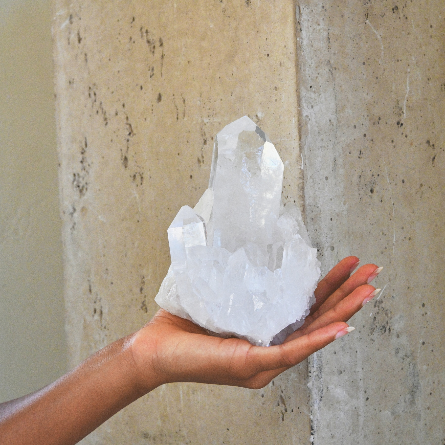 Clear quartz cluster held against travertine wall
