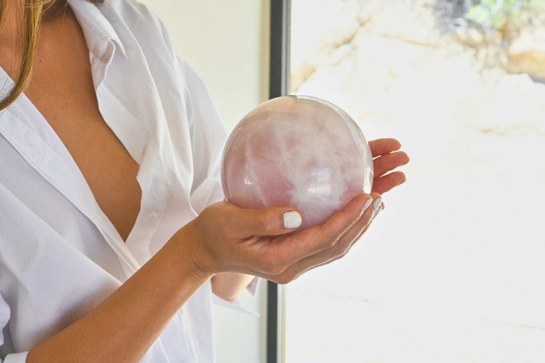Rose quartz sphere held in hands, white shirt, window light