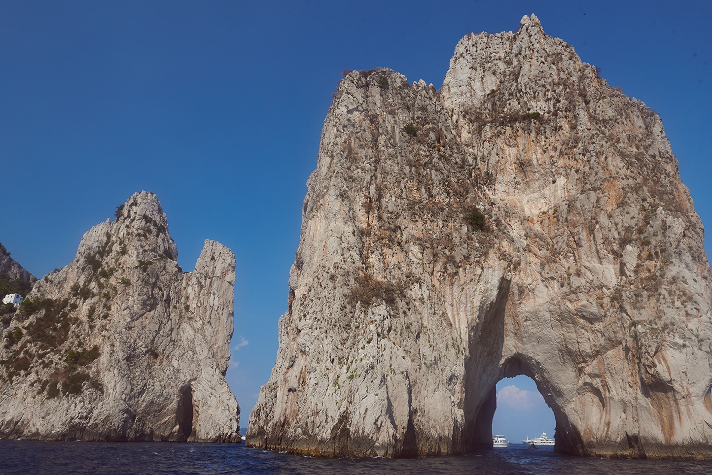Faraglioni rocks from sea level, natural arch, deep blue sky, boat passing through