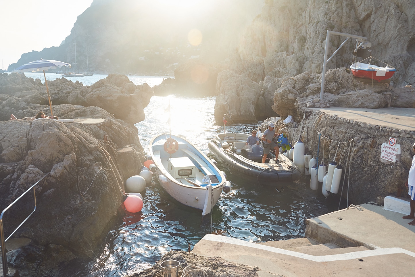 Capri rocky harbor, fishing boats moored between cliff walls, golden backlight on water