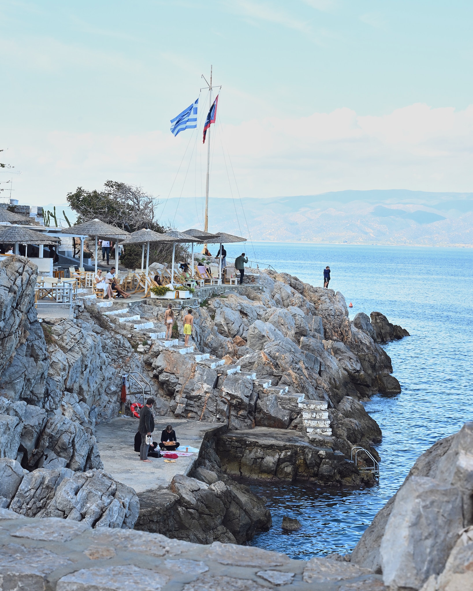 Hydra rocky beach bar, Greek flag, blue Aegean