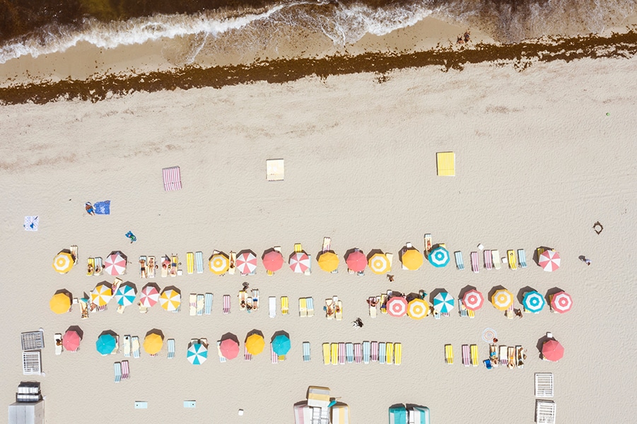 Beach umbrellas from directly above, colorful rows on white sand, Slim Aarons palette