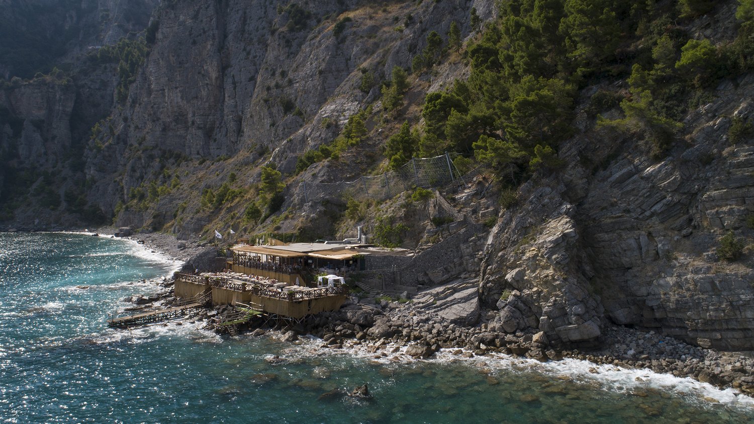 Cliffside beach restaurant from above, turquoise cove, dramatic rock face