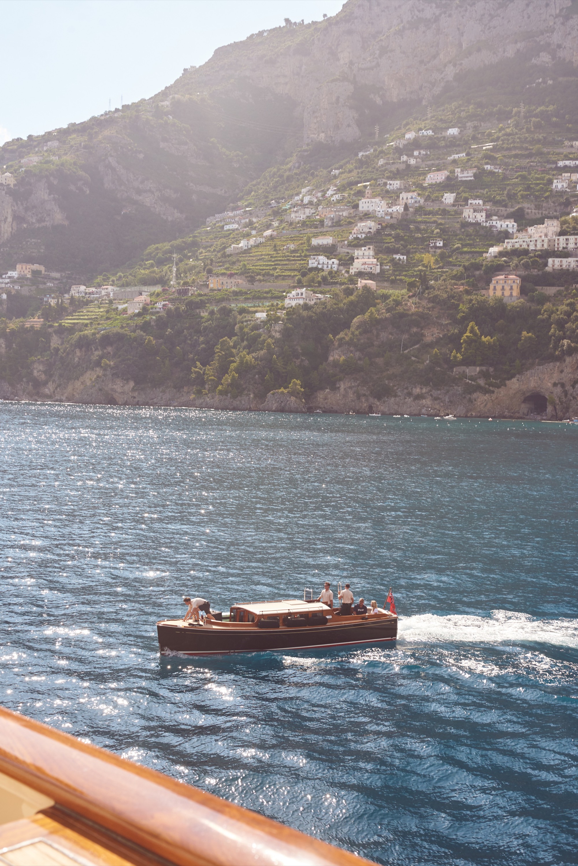 Amalfi wooden boat from yacht deck, turquoise water, coastline behind