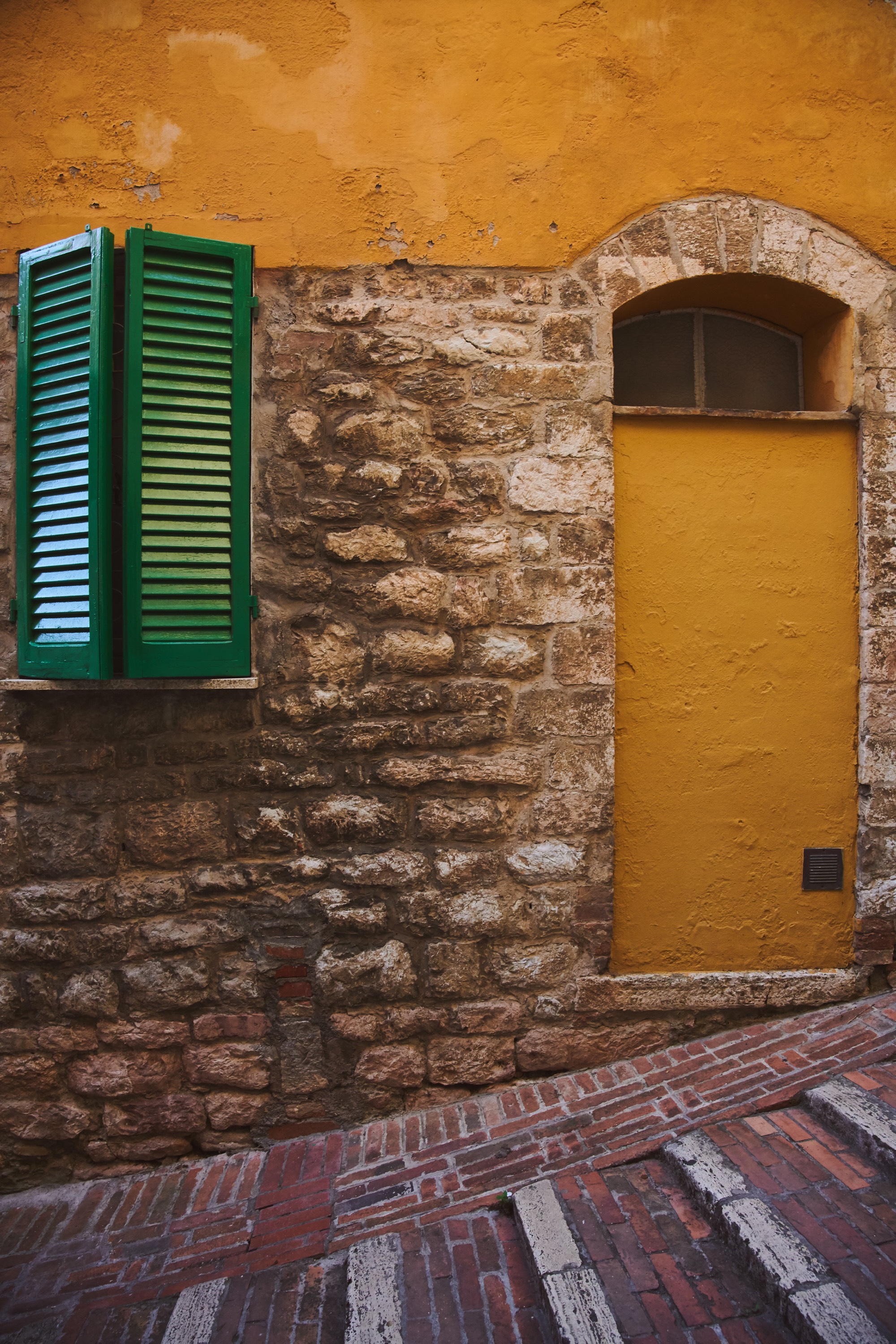 Umbrian stone facade, green shutters, ochre wall, worn brick steps