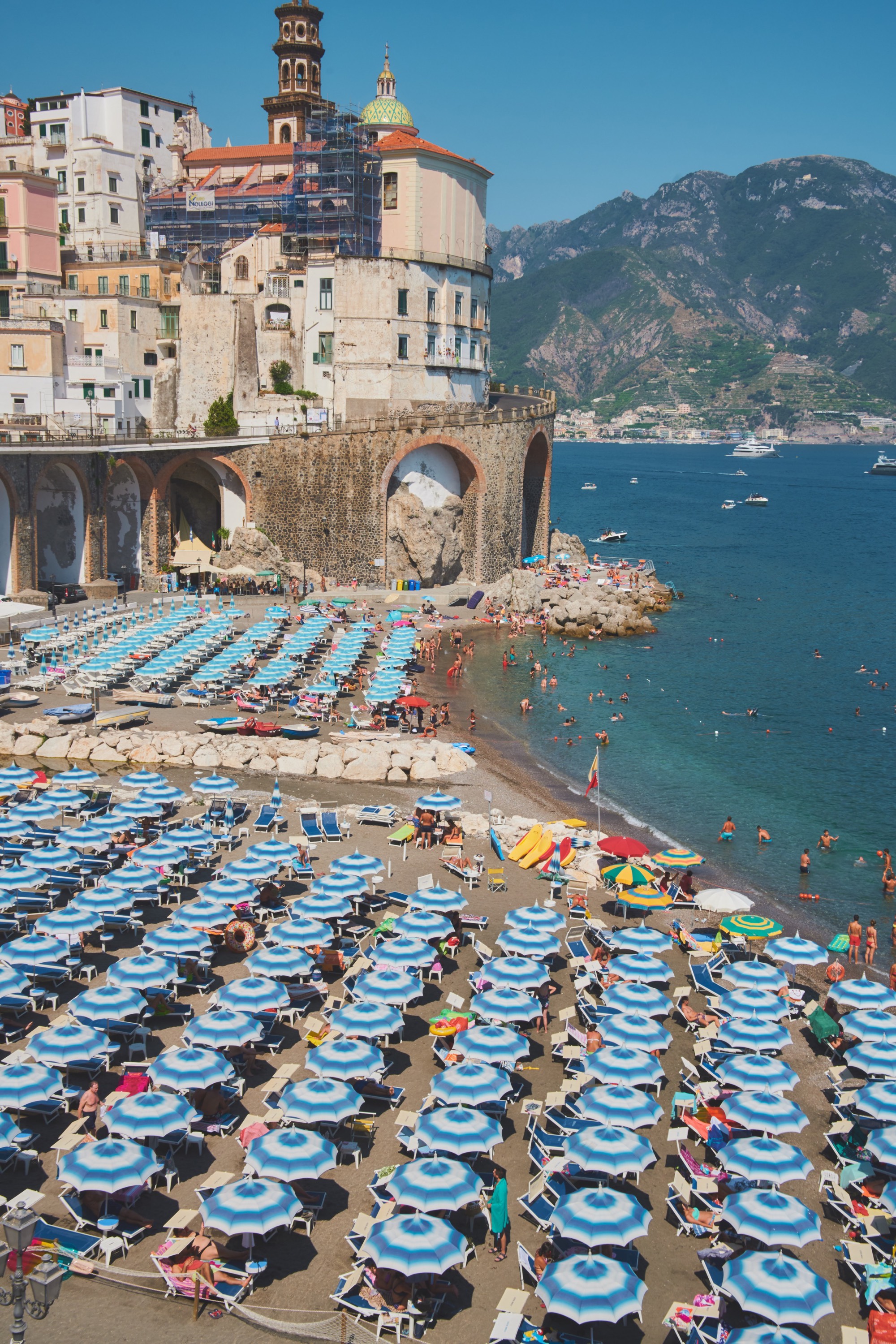 Atrani beach, rows of blue and white striped umbrellas, medieval tower and church
