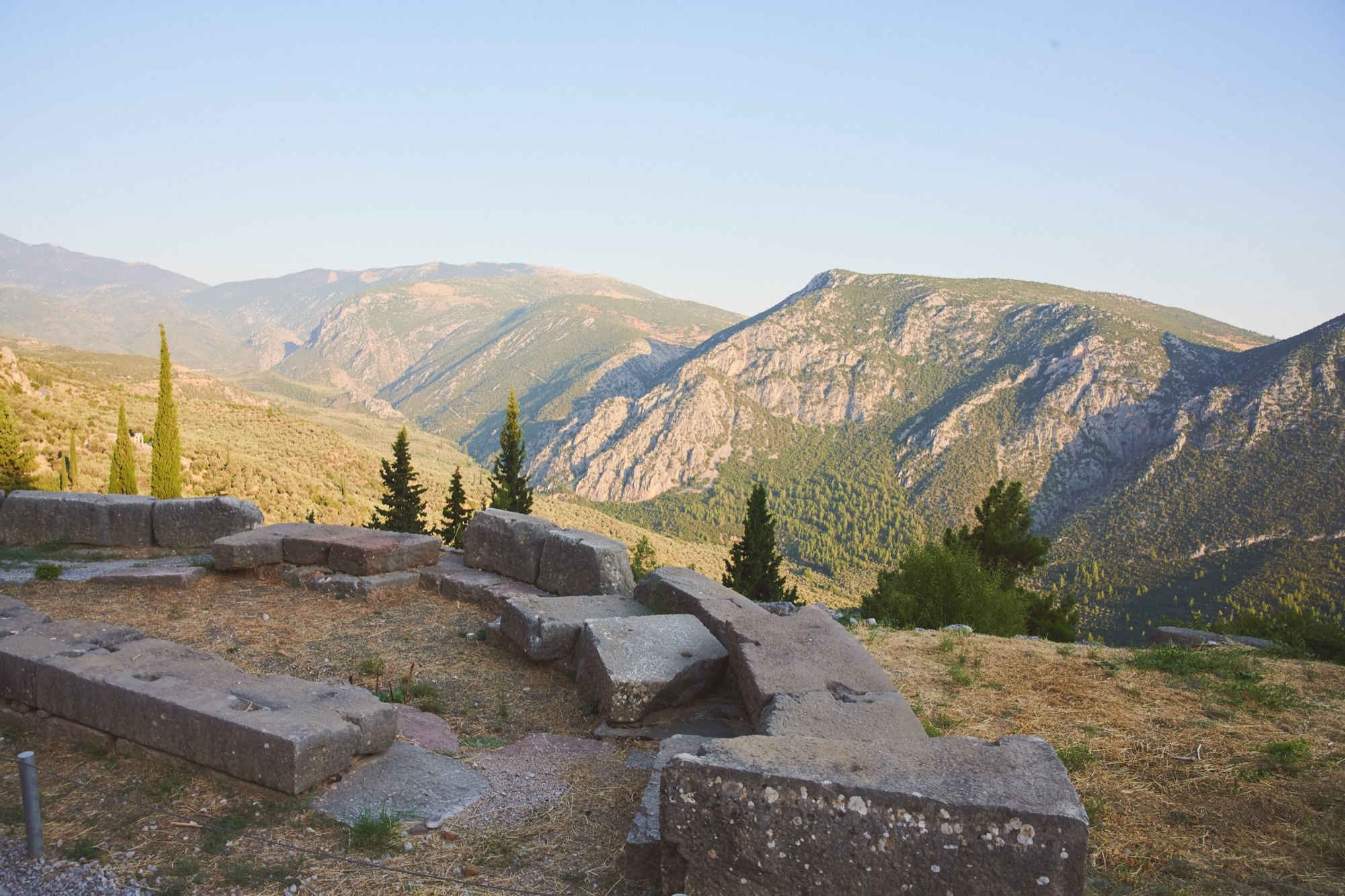 Delphi mountain vista, ancient stone ruins in foreground, cypress and valley beyond